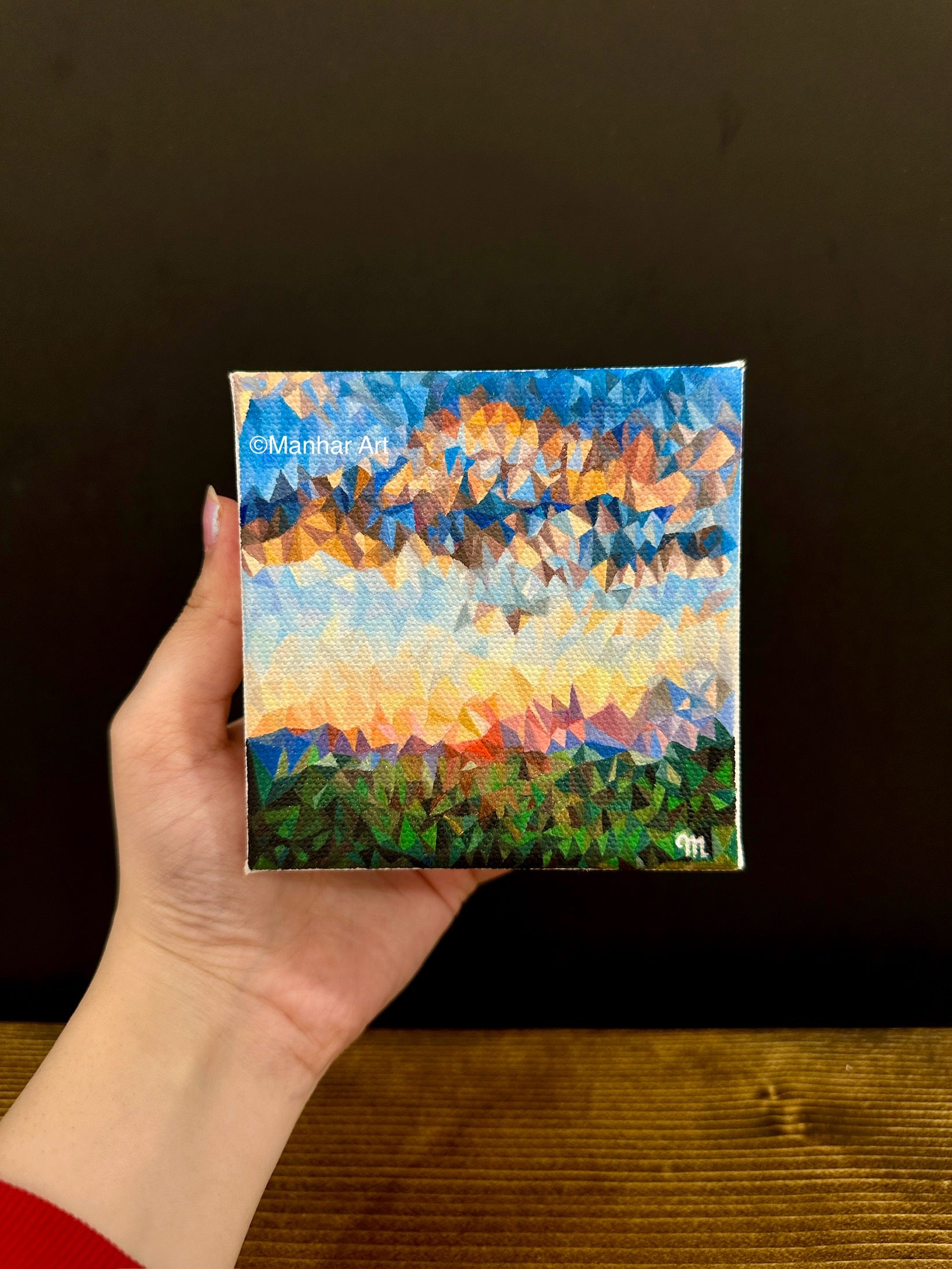 Artist showing the 4x4 inches, 10.1x10.1cm oil painting of a bright orange sunrise over a green field, set against a deep blue sky with clouds, rendered in a unique triangles art style, ideal for home decor.